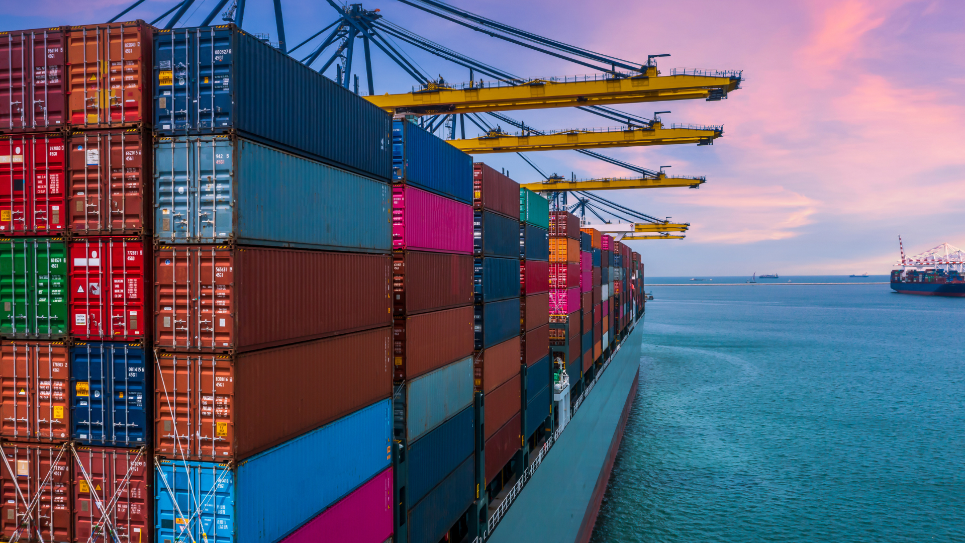 A loading computer enabled container ship under a sunset sky.