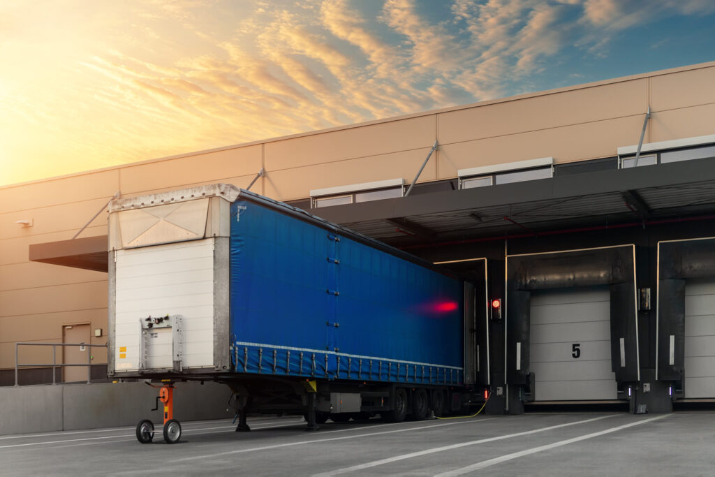 Innovative modern logistics warehouse center complex building exterior bay gate semi-trailer unloading goods distribuition warm blue sunset sky background. Cargo storage facility industry building